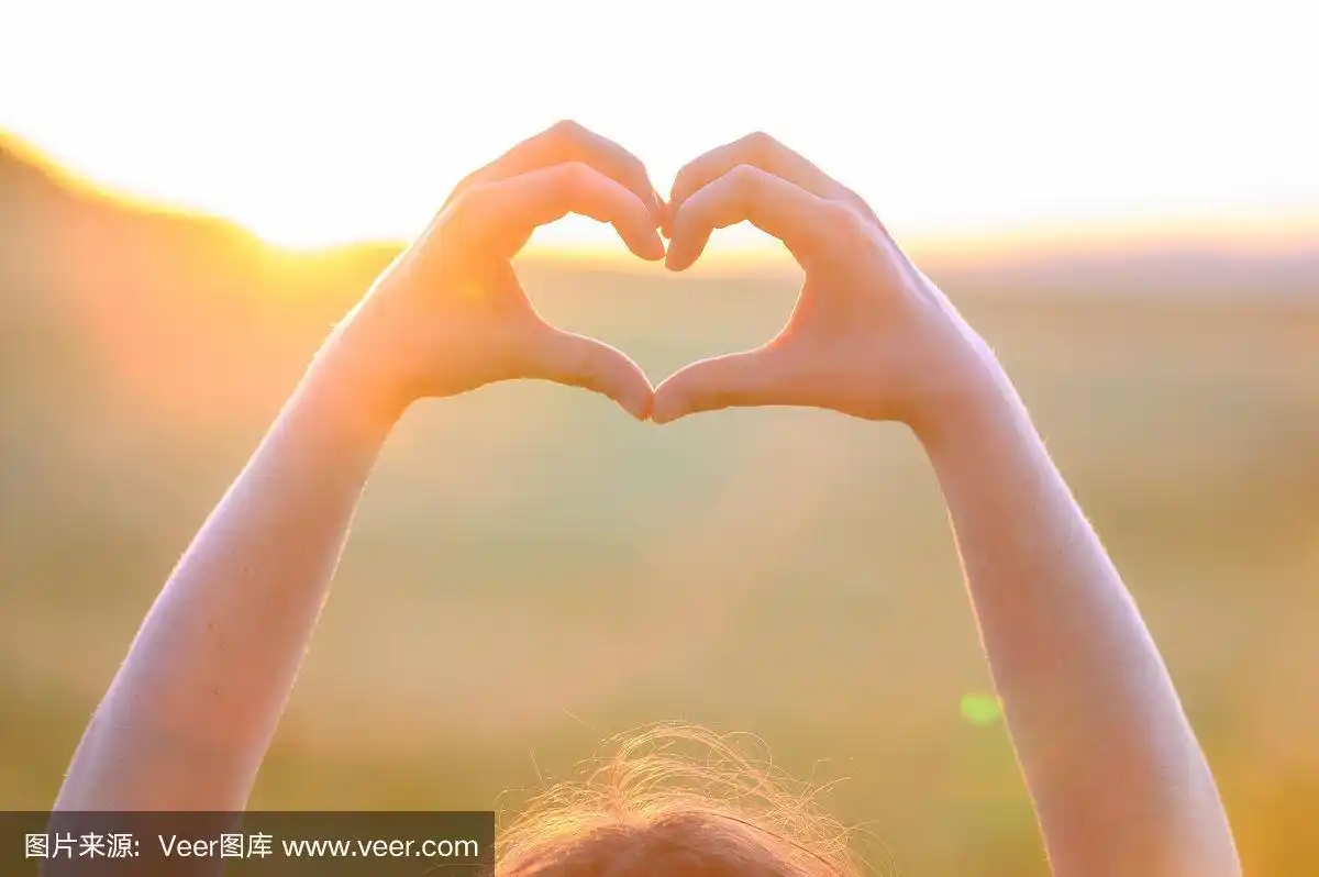 手在夕阳下做心形.女人的手做心形手势的特写.