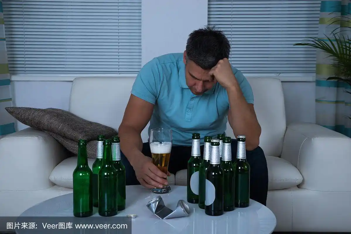 一个男人晚上坐在沙发上喝啤酒