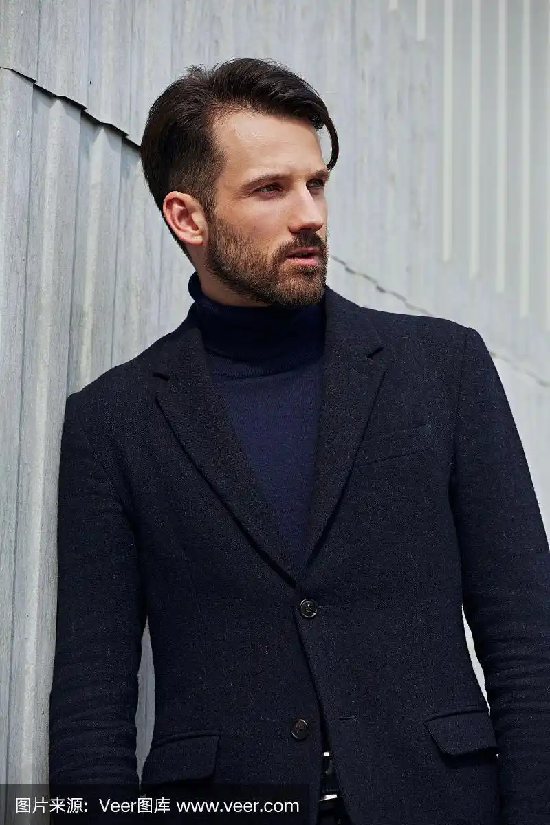 时尚胡须风格的商业英俊男模特在风格服装蓝色夹克摆姿势在街头墙户外