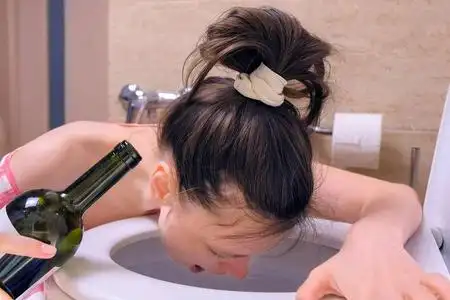 拿着酒瓶醉汉在厕所里呕吐坐在地上,手里拿着酒瓶,早上宿醉,侧视.照片