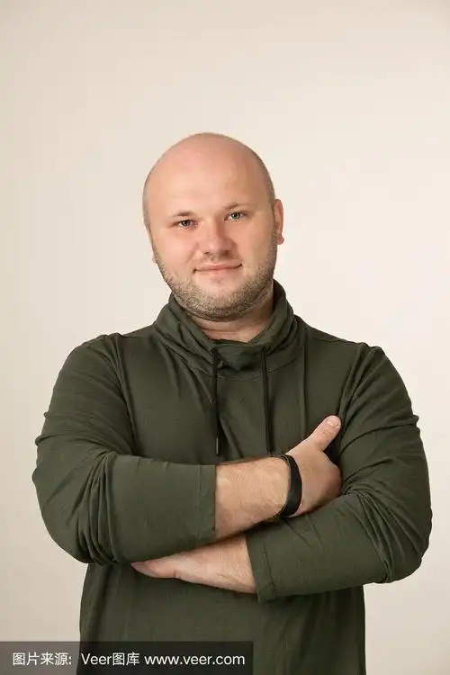 一个35岁剃着光头的大胡子男人的工作室肖像,在米色的背景上穿着绿色