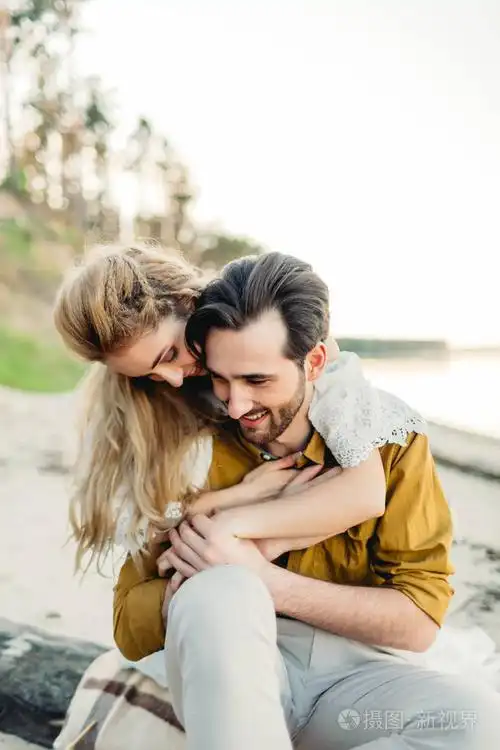 一对年轻夫妇拥抱在沙滩上.美丽的女孩拥抱她的男友从后面.婚礼走.