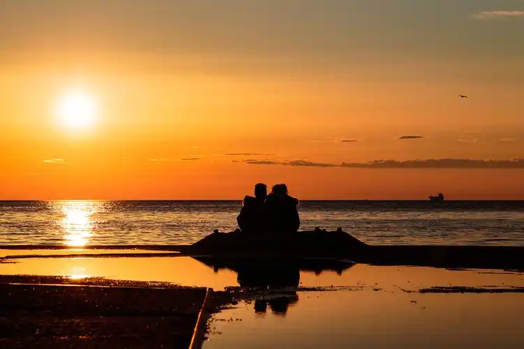 一对年轻夫妇在的海边看美丽的夕阳看日落浪漫的情侣
