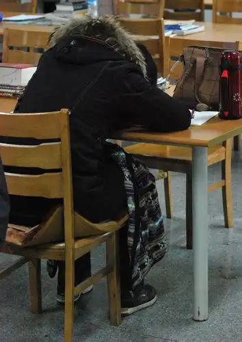 一位有些疲劳的学生趴在桌子上休息,腿上甚至盖了毯子
