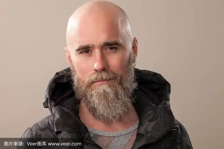 一名40岁剃着光头,穿着黑色棉袄,米色背景的留胡子男子的工作室肖像