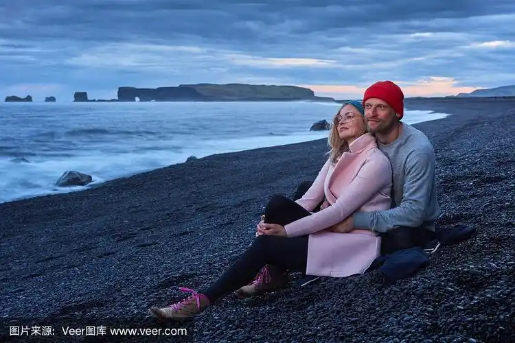 一对情侣依偎在一起坐在海滩上.日落