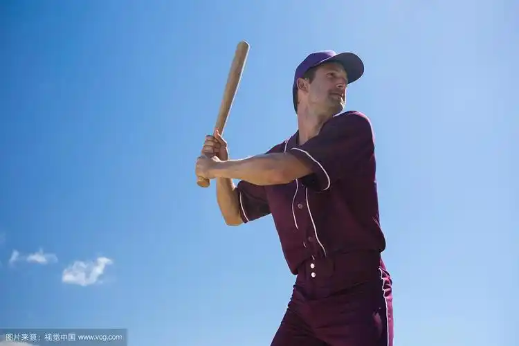 在阳光明媚的日子里,年轻的棒球运动员拿着球棒对抗蓝天的低角度视图